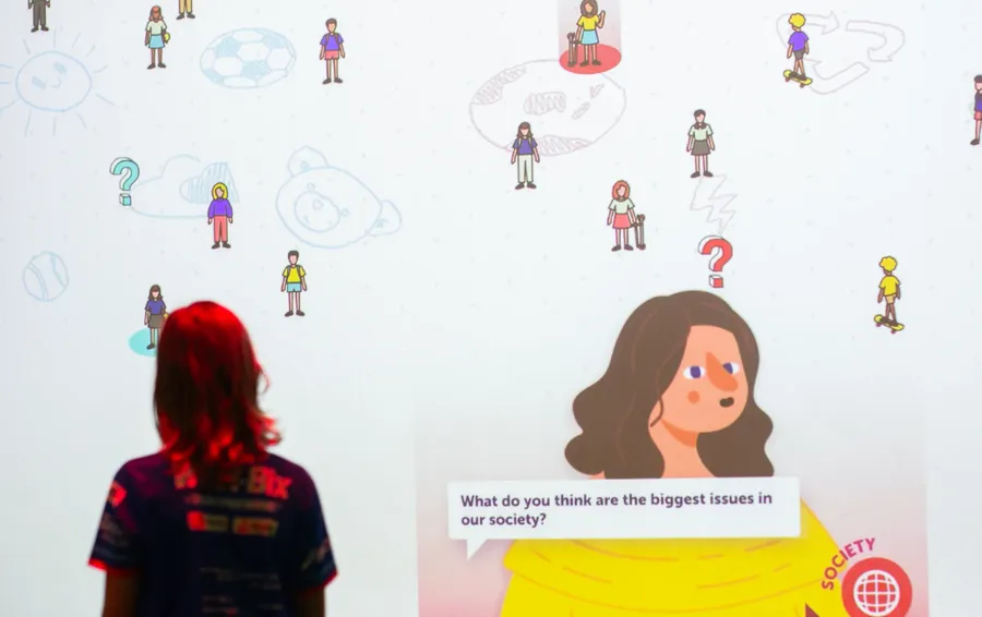 Image of girl standing under a red spotlight and reading the experience of a child on the screen
